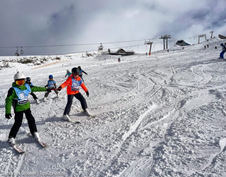 Kinderen oefenen skiën in blauwe groep met skileraar in Oostenrijk