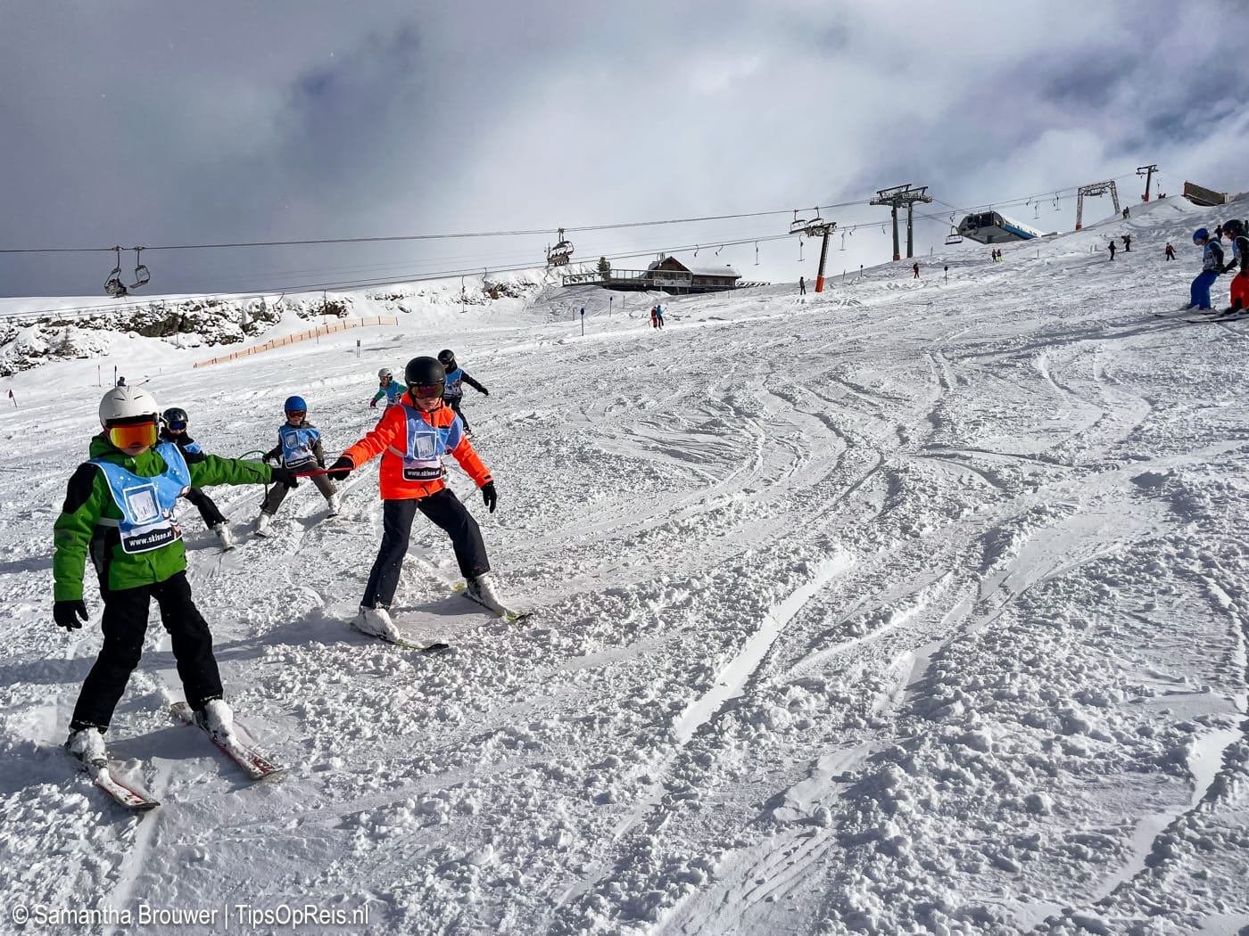 Kinderen oefenen skiën in blauwe groep met skileraar in Oostenrijk